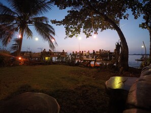 A wooden deck overlooking a body of water, surrounded by palm trees and street lamps.