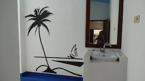 A bathroom with a white sink, a blue bathtub, and a wall mural of a palm tree and waves. - Villa Bintang (Gili Trawangan)