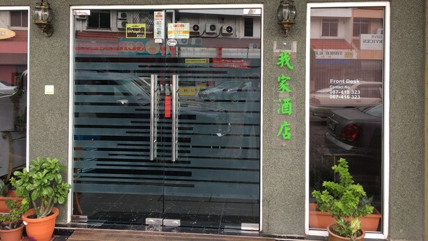 The exterior of the Micasa Hotel with a large glass entrance, a sign indicating a contact number, and a small sign with a date. - Micasa Hotel (Labuan)