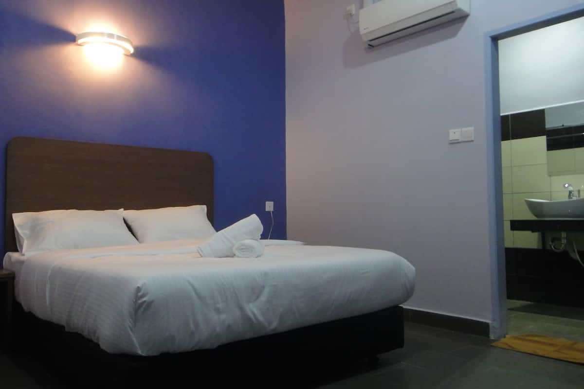 A hotel room with a bed, nightstand, wall-mounted air conditioner, and a bathroom with a sink and mirror.