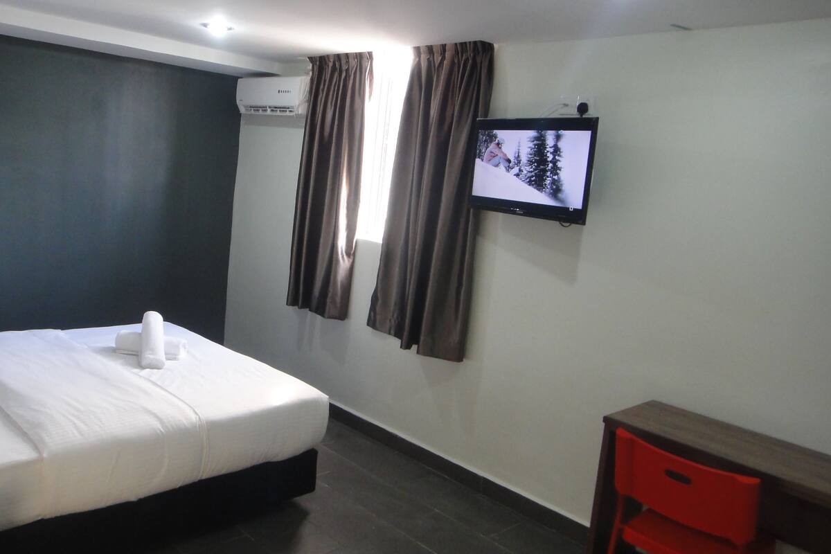 A hotel room with a bed, a TV mounted on the wall, and a desk with a chair.