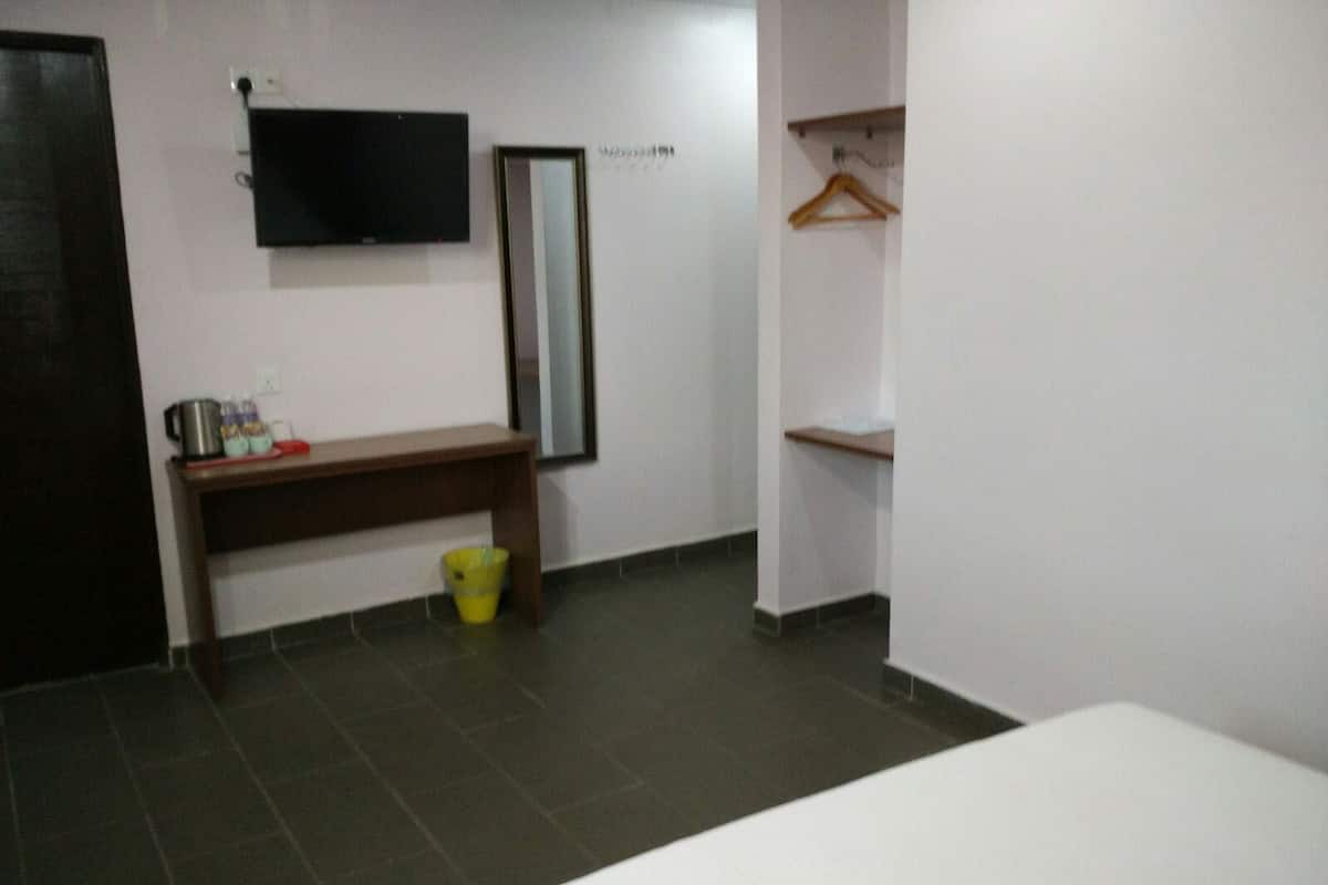 A room with a bench, a television mounted on the wall, a mirror, and a small shelf with a hanger.