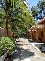 Un sentier mène à un bâtiment à toit de chaume, entouré d’une clôture en bois et agrémenté de plantes en pot.