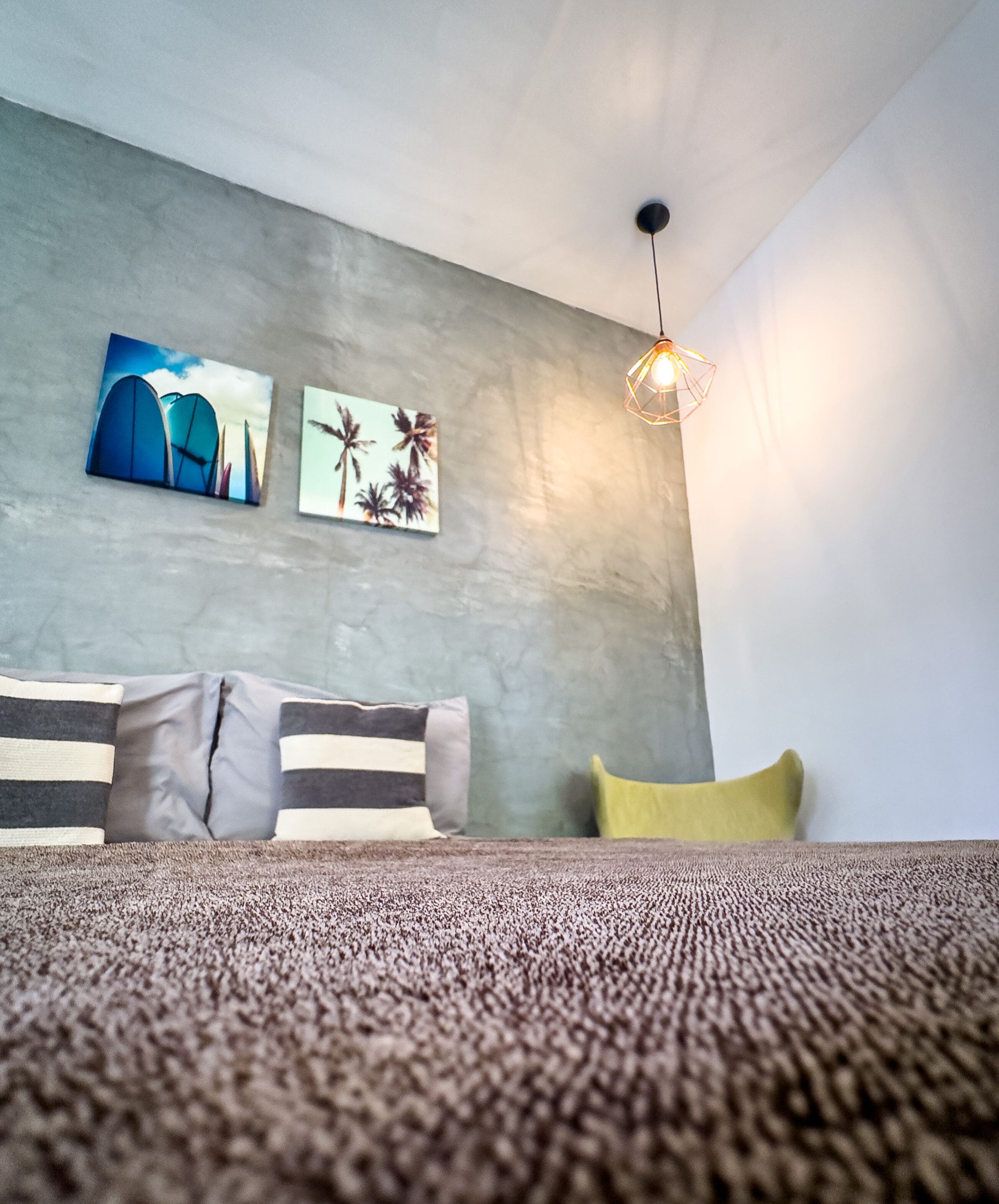 A modern living room with a gray sofa, a yellow pillow, and two wall art pieces depicting architectural structures and palm trees.