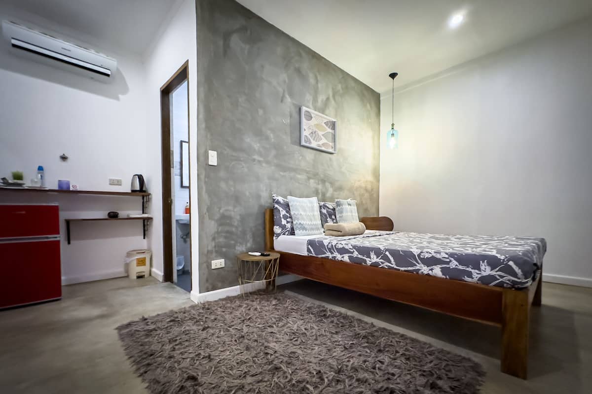 Um quarto com uma cama, uma escrivaninha pequena, um frigorífico vermelho e um tapete fofo cinzento.