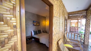 A room with a bed, a nightstand, a wall-mounted picture, and a balcony with a chair. - Alona Pawikan (Panglao)