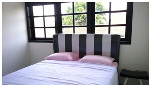 A bed with white bedding and pink pillows, a black and white striped headboard, and a small stool beside the bed. - Mess Inn Semarang (Semarang)