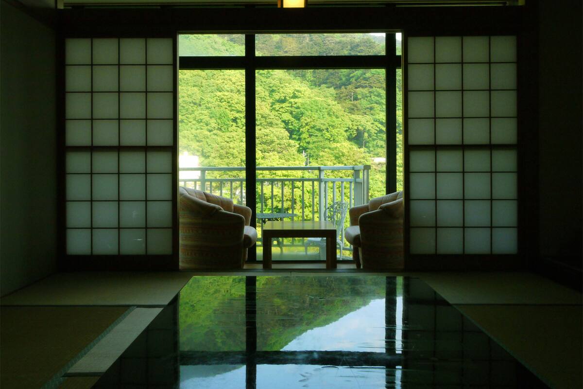 Habitació amb paviment de tatami, una taula baixa, dues cadires i vista a un bosc verd i exuberant a través de grans portes corredisses.