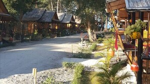 A row of wooden cabins with thatched roofs, surrounded by dense trees and a gravel path. - Eco Lanta Hideaway Beach Resort (Ko Lanta)