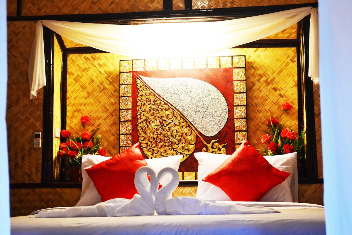 Une chambre d’hôtel avec un lit, des oreillers rouges et blancs, un mur décoratif et un vase rempli de fleurs rouges.