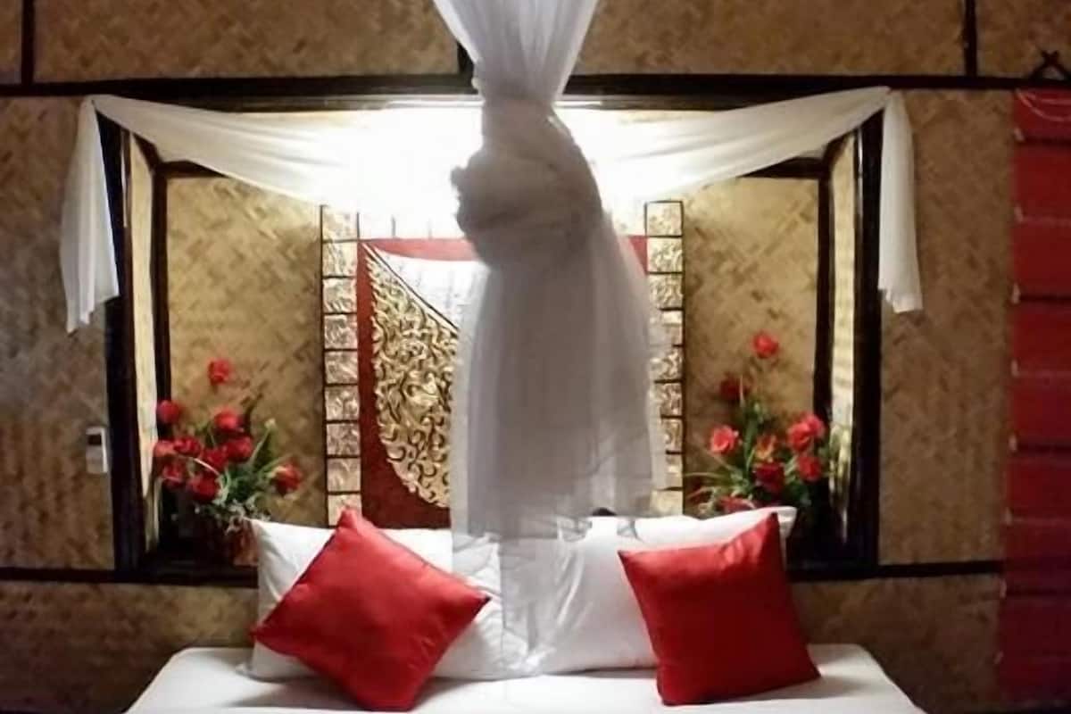 Un lit à baldaquin, des oreillers rouges et une composition décorative de serviettes disposées sur le lit.