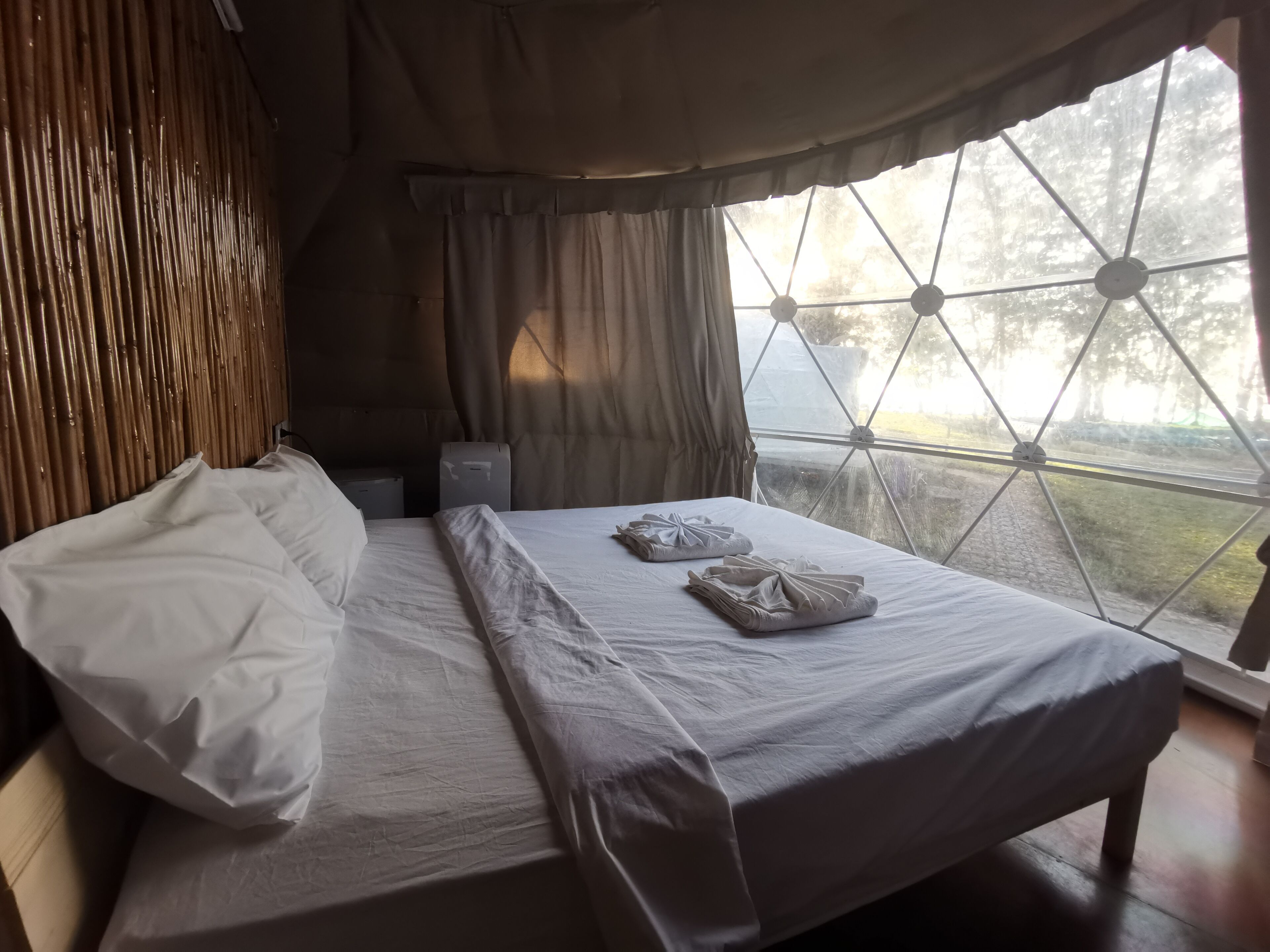 Una cama con ropa blanca, cabecera de madera y una ventana con diseño geométrico.