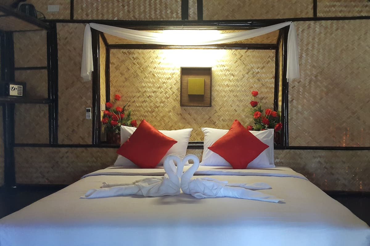 Une chambre d’hôtel avec un lit, du linge de lit blanc, des oreillers rouges, un ensemble de serviettes blanches disposées avec soin, une lampe fixée au mur et un tableau encadré.