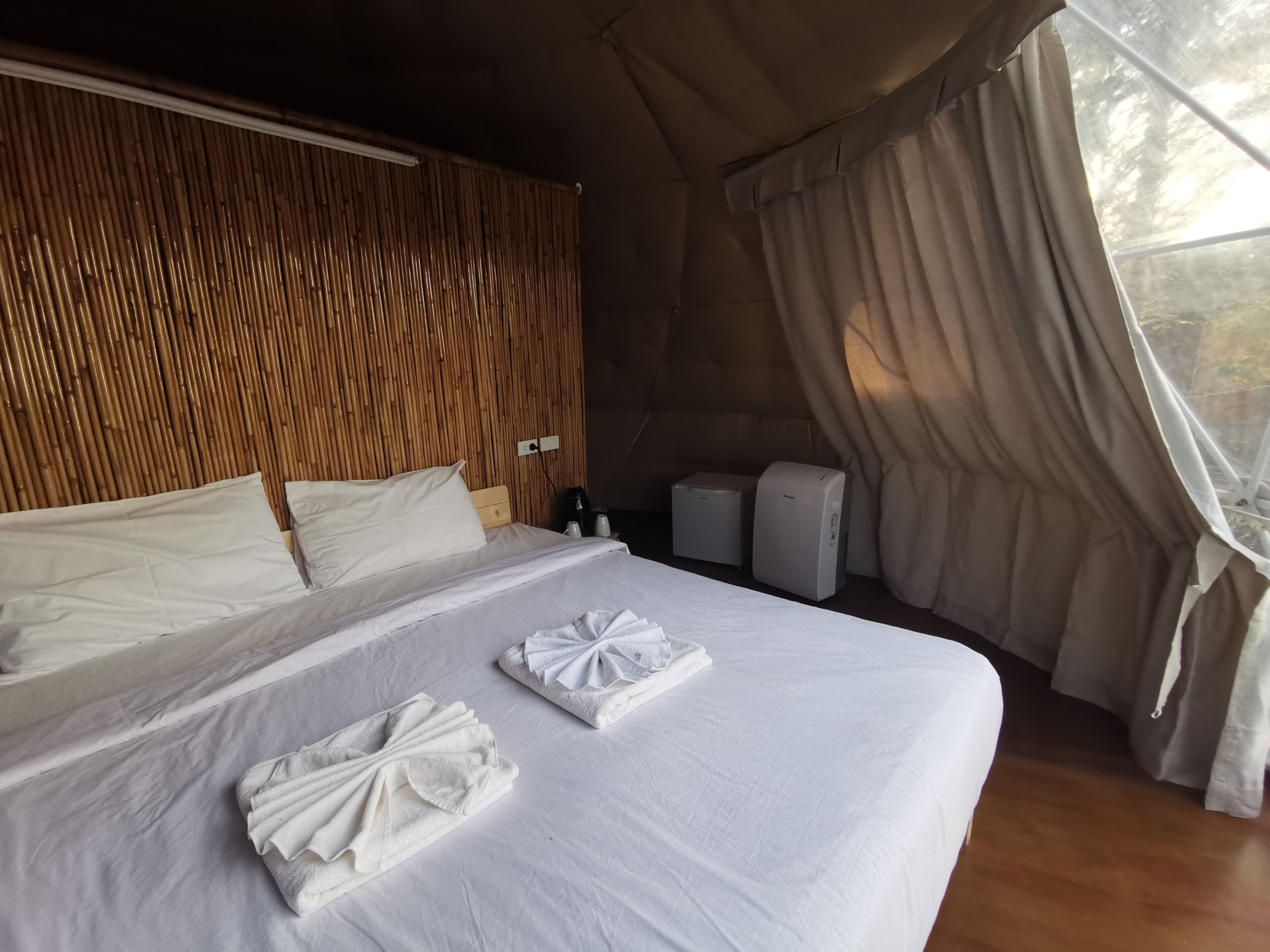 A bed with white linens and towels, a wooden headboard, and a window with curtains.