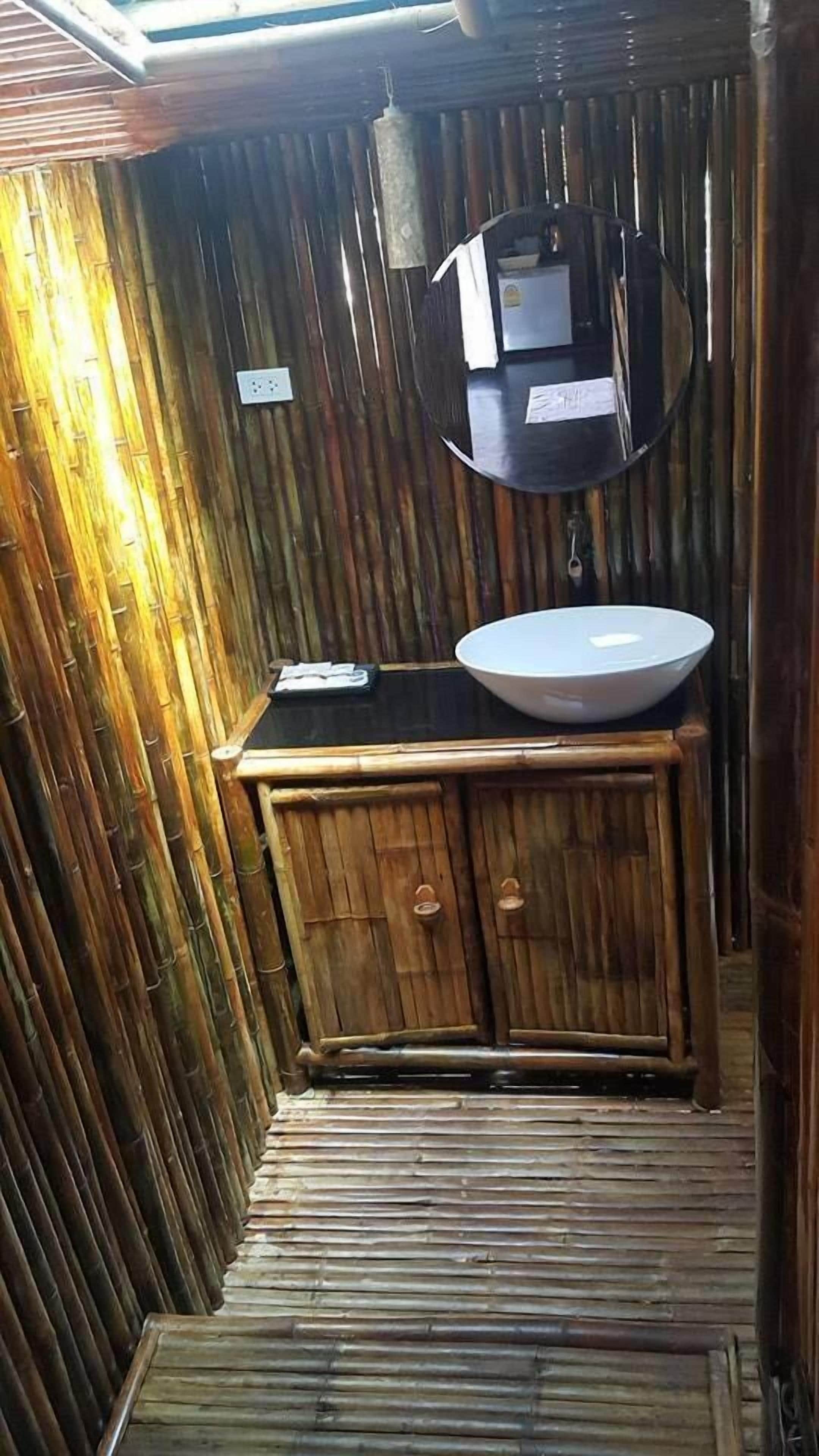 A bamboo-walled bathroom with a sink and mirror.