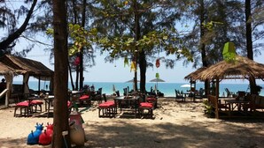 A beachside restaurant with outdoor seating, tables, and chairs, surrounded by trees and overlooking the sea. - Eco Lanta Hideaway Beach Resort (Ko Lanta)