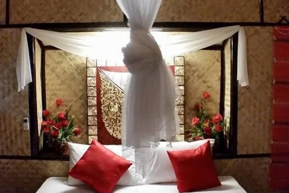 Un lit à baldaquin, des oreillers rouges et un objet décoratif ressemblant à un visage, placé sur le couvre-lit.