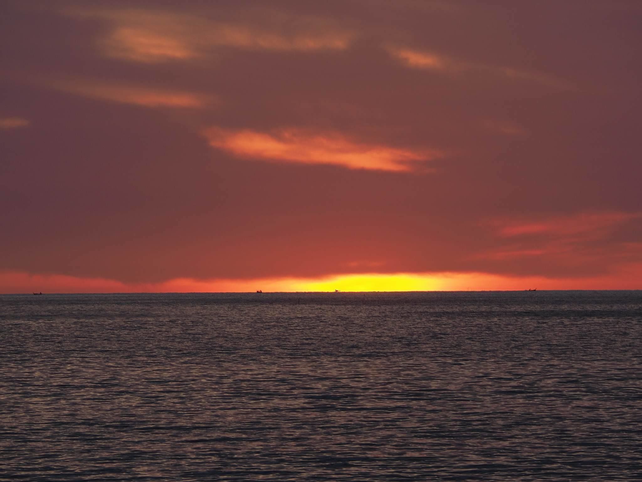 Um pôr do sol sobre um mar calmo, com horizonte límpido.