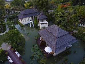 A traditional-style building with a tiled roof, surrounded by lush greenery and a small pond.