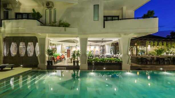 A modern hotel with a large indoor swimming pool, multiple floors, and outdoor seating areas. - Central Suite Residence (Siem Reap)