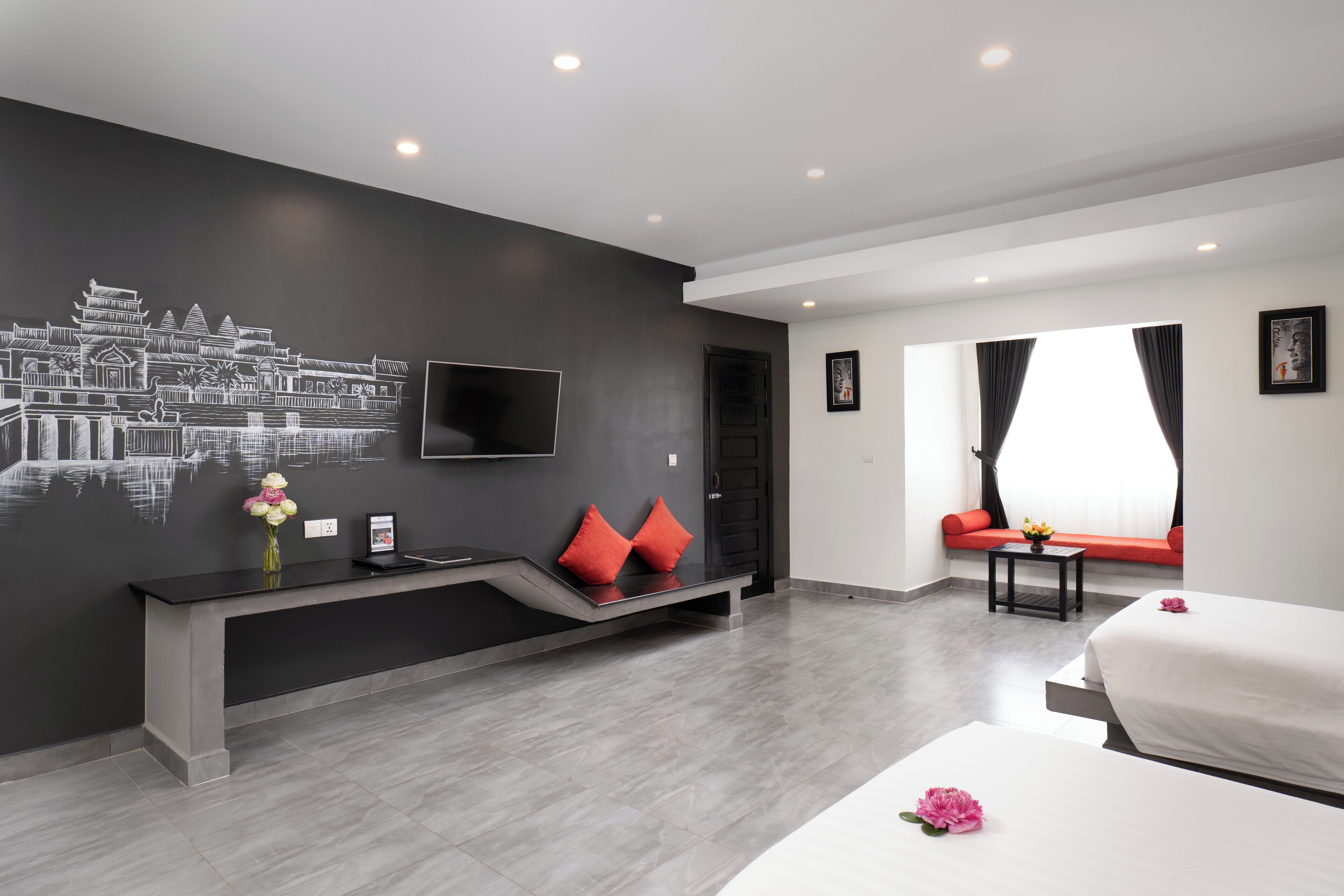A modern hotel room with a large bed, a desk with a flat-screen TV, a bench with red cushions, and a wall mural.