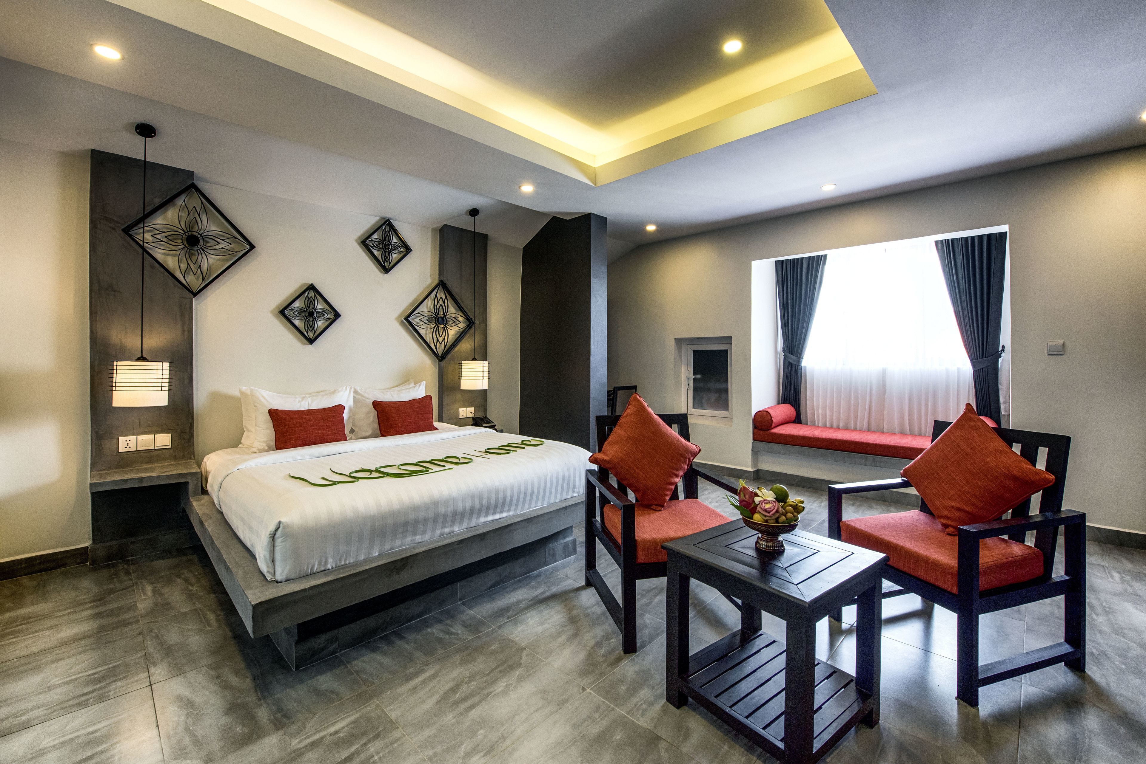 Una habitación de hotel moderna con una cama grande, dos sillones, una mesita y decoración en la pared.