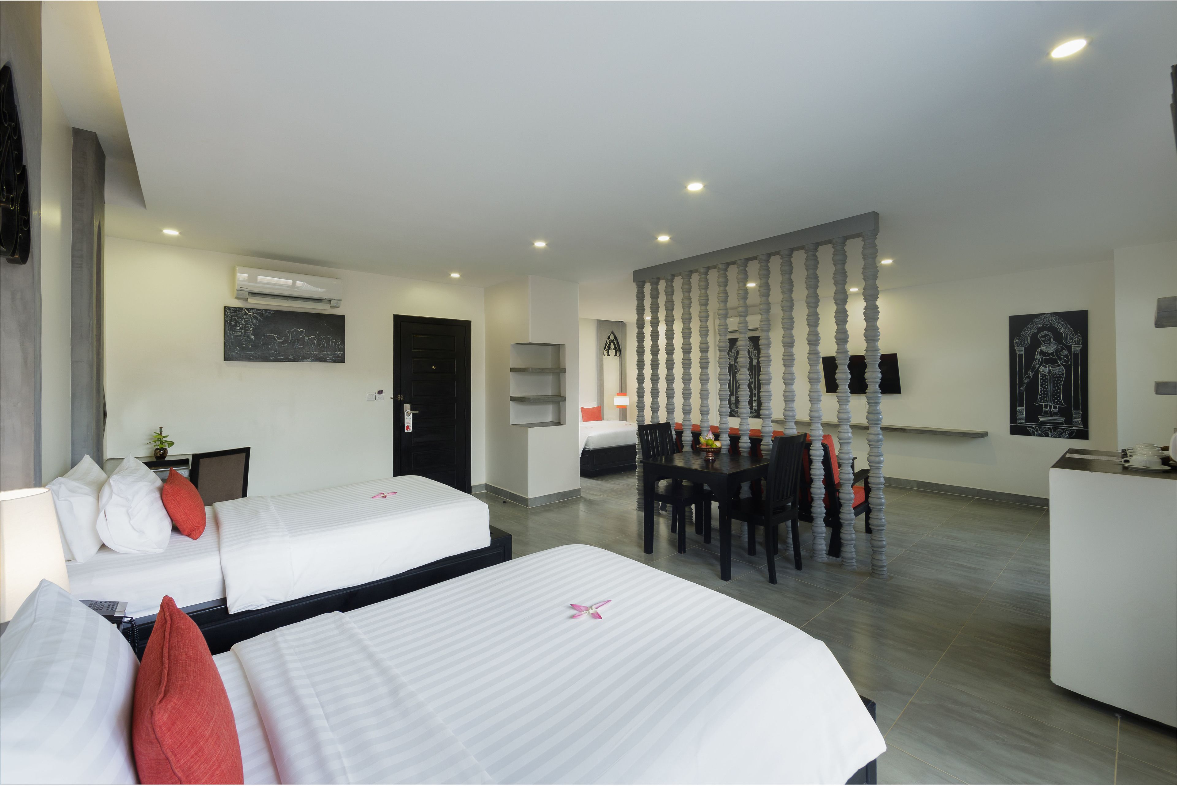 A hotel room with two beds, a dining area, and a reception desk.