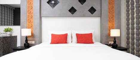 A modern hotel room with a large bed, two red pillows, a grey headboard with decorative panels, and a nightstand with a lamp and a small plant.