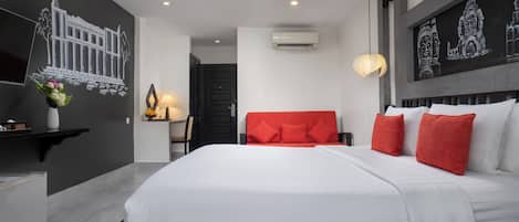 A modern hotel room with a large bed, red and white pillows, a wall-mounted air conditioner, and a decorative wall piece.