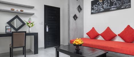 Una sala de estar moderna con un sofá negro, cojines rojos, una mesa de centro con un frutero, un espejo con marco negro y una obra de arte colgada en la pared que representa elefantes.