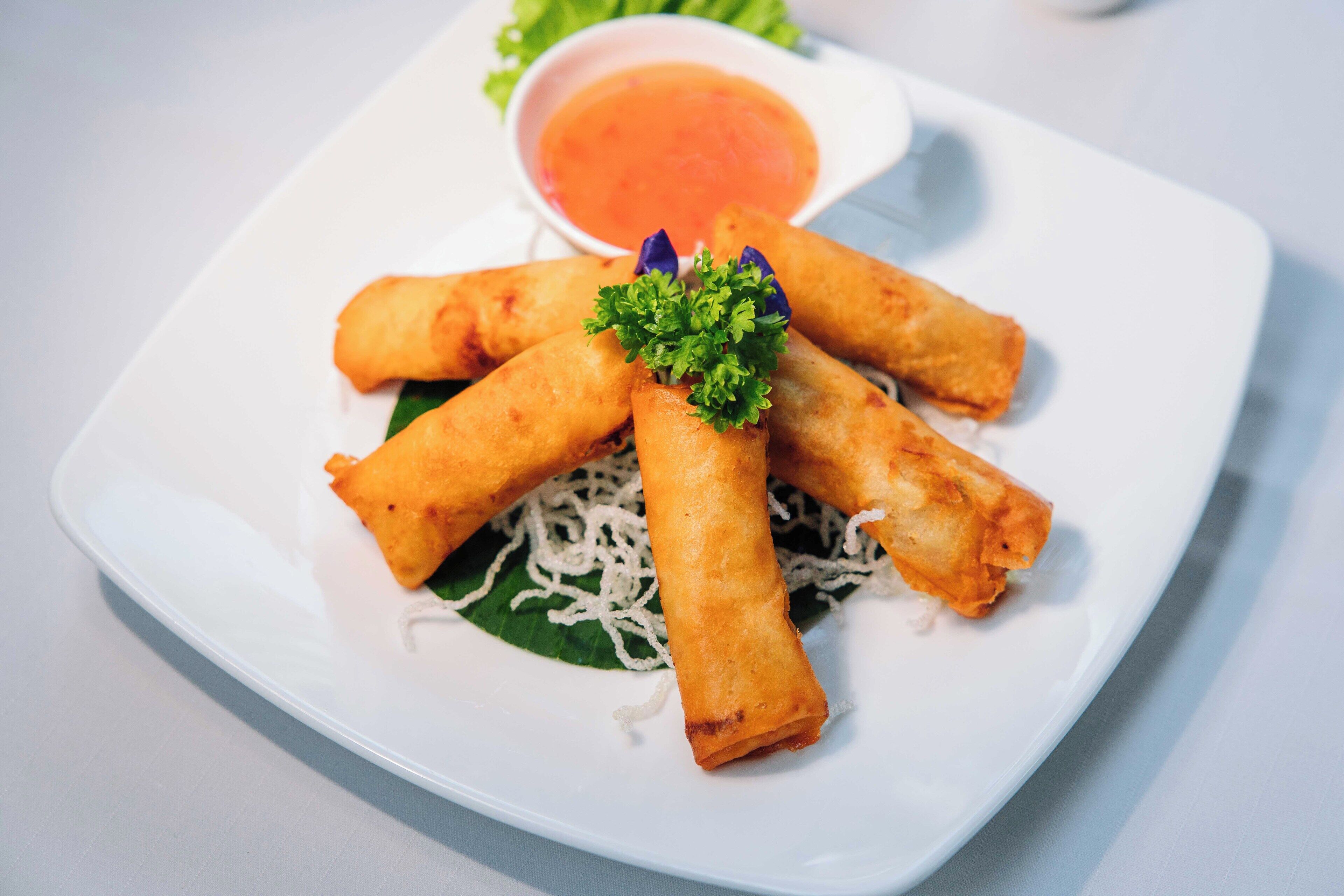 A plate of spring rolls with a side of dipping sauce and garnish.