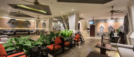 A spacious lobby with multiple seating areas, ceiling fans, and a television screen.