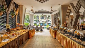 A buffet setup with multiple serving stations, tables, and chairs arranged in a spacious room with a high ceiling and decorative wall panels. - Central Suite Residence (Siem Reap)