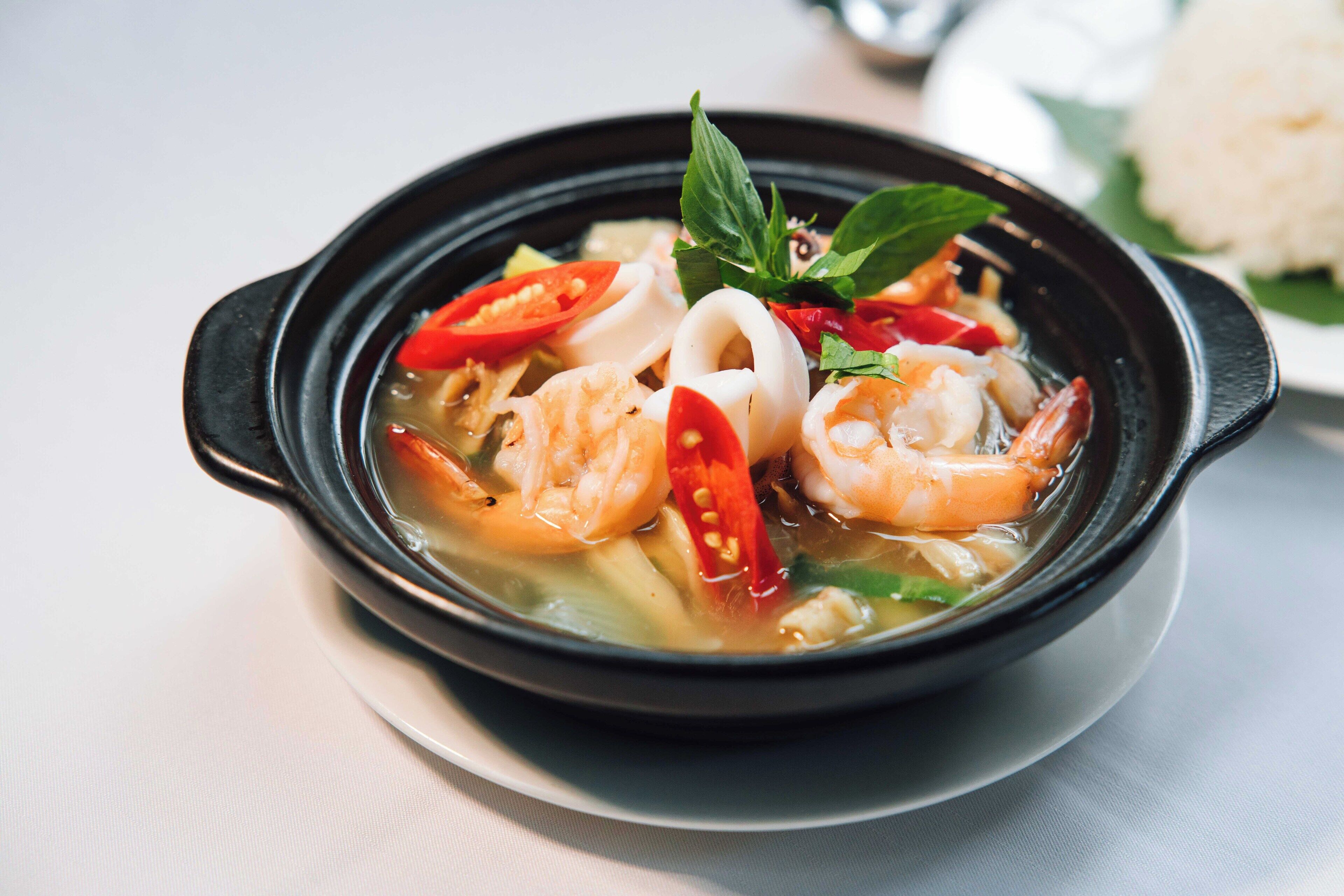 A bowl of soup with shrimp, vegetables, and herbs.
