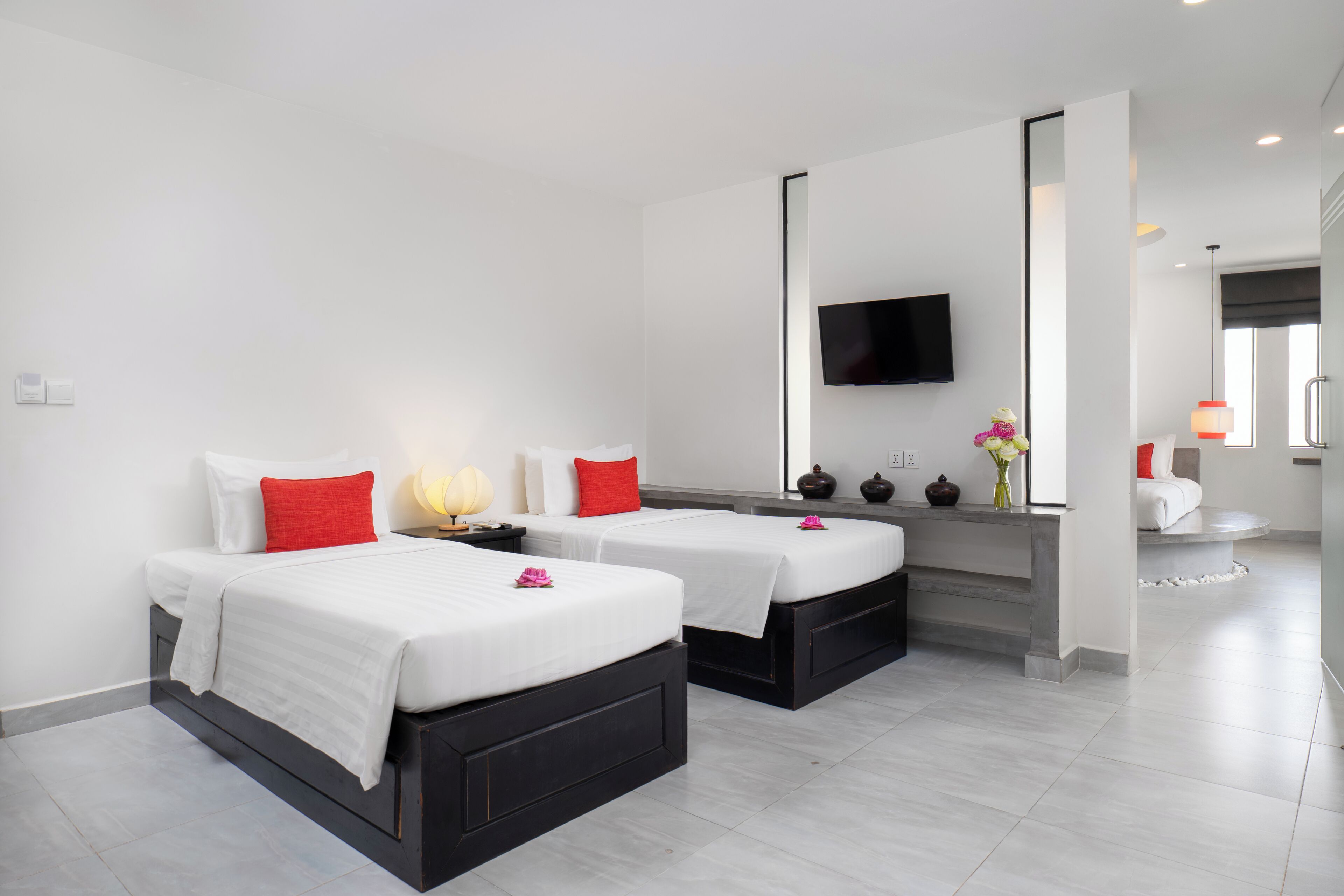 A hotel room with two beds, a TV, and a desk with a vase of flowers.