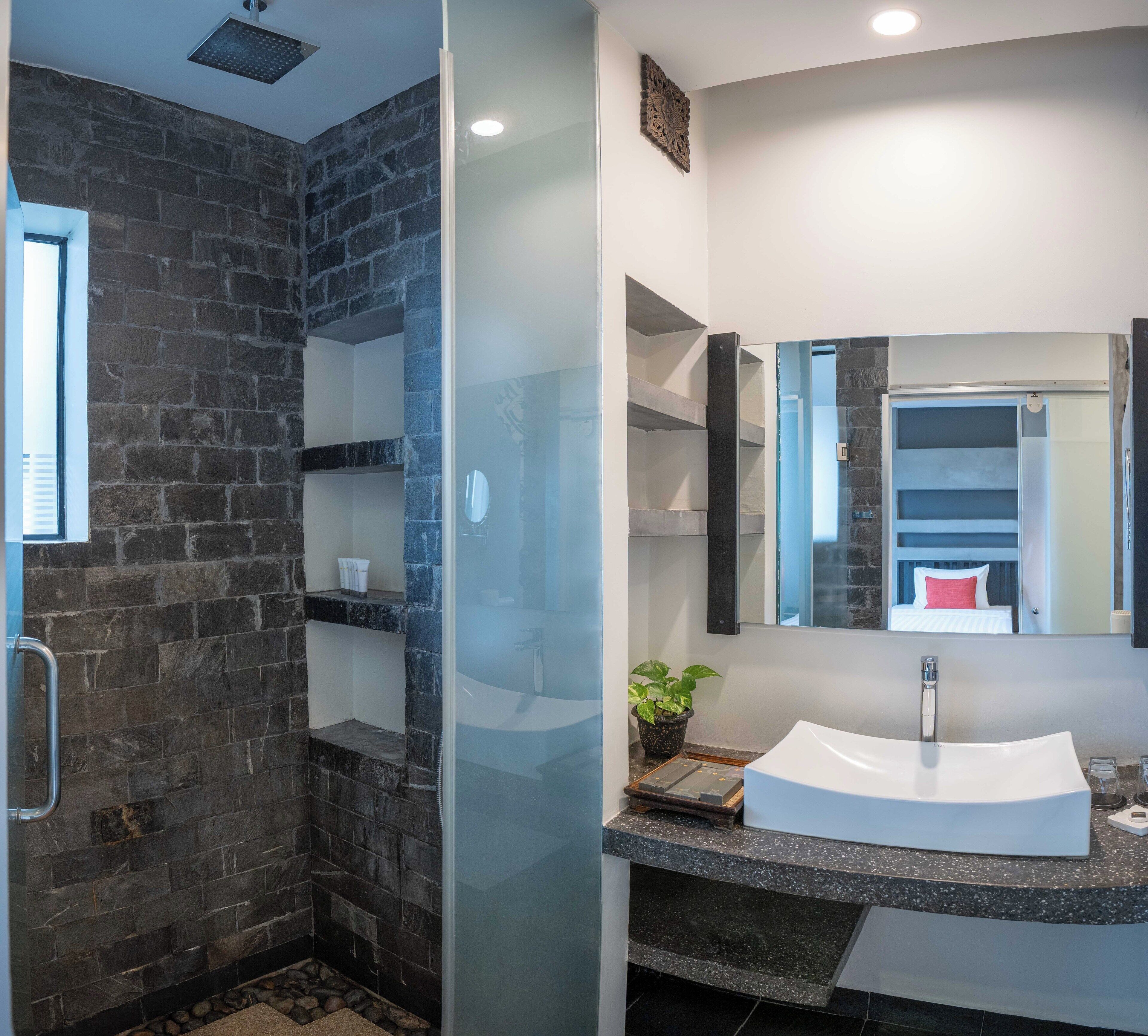 A modern bathroom with a stone wall shower, a glass-enclosed walk-in shower, a white sink, and a large mirror.