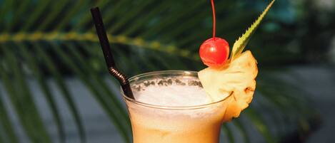 A tall glass with a pineapple garnish and a cherry on top, placed on a dark surface with a blurred green background.