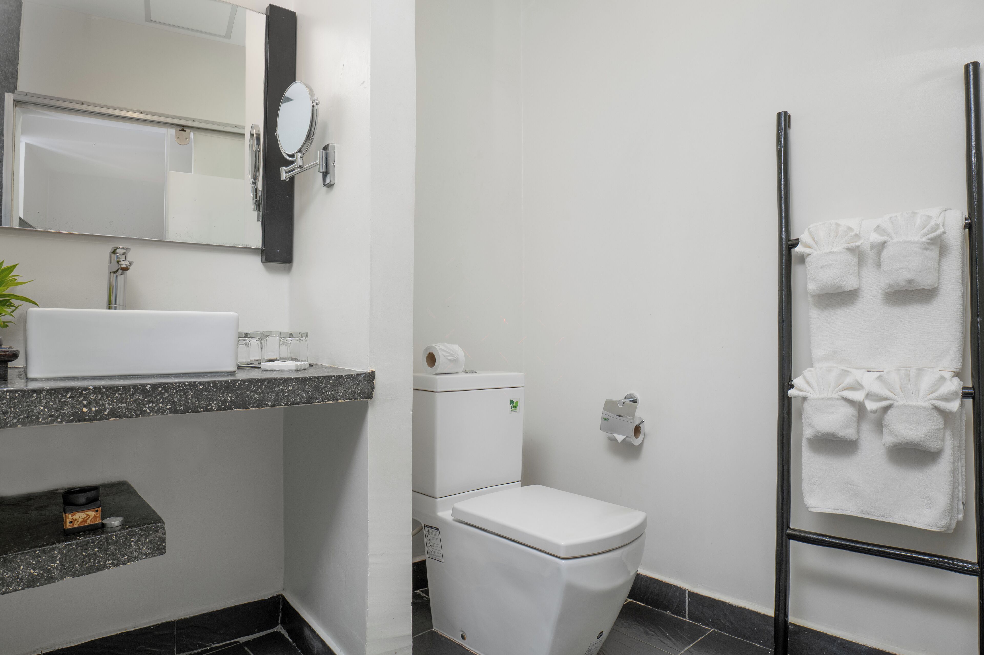 A modern bathroom with a white toilet, a sink with a mirror, and a towel rack with towels.