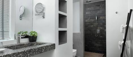 A modern bathroom with a granite countertop, two wall-mounted mirrors, a toilet, a shower with a stone wall, and a towel rack.