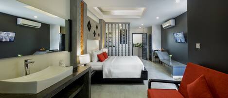 Habitación de hotel moderna con una bañera grande, una cama con almohadas rojas, un sofá y un televisor en la pared.