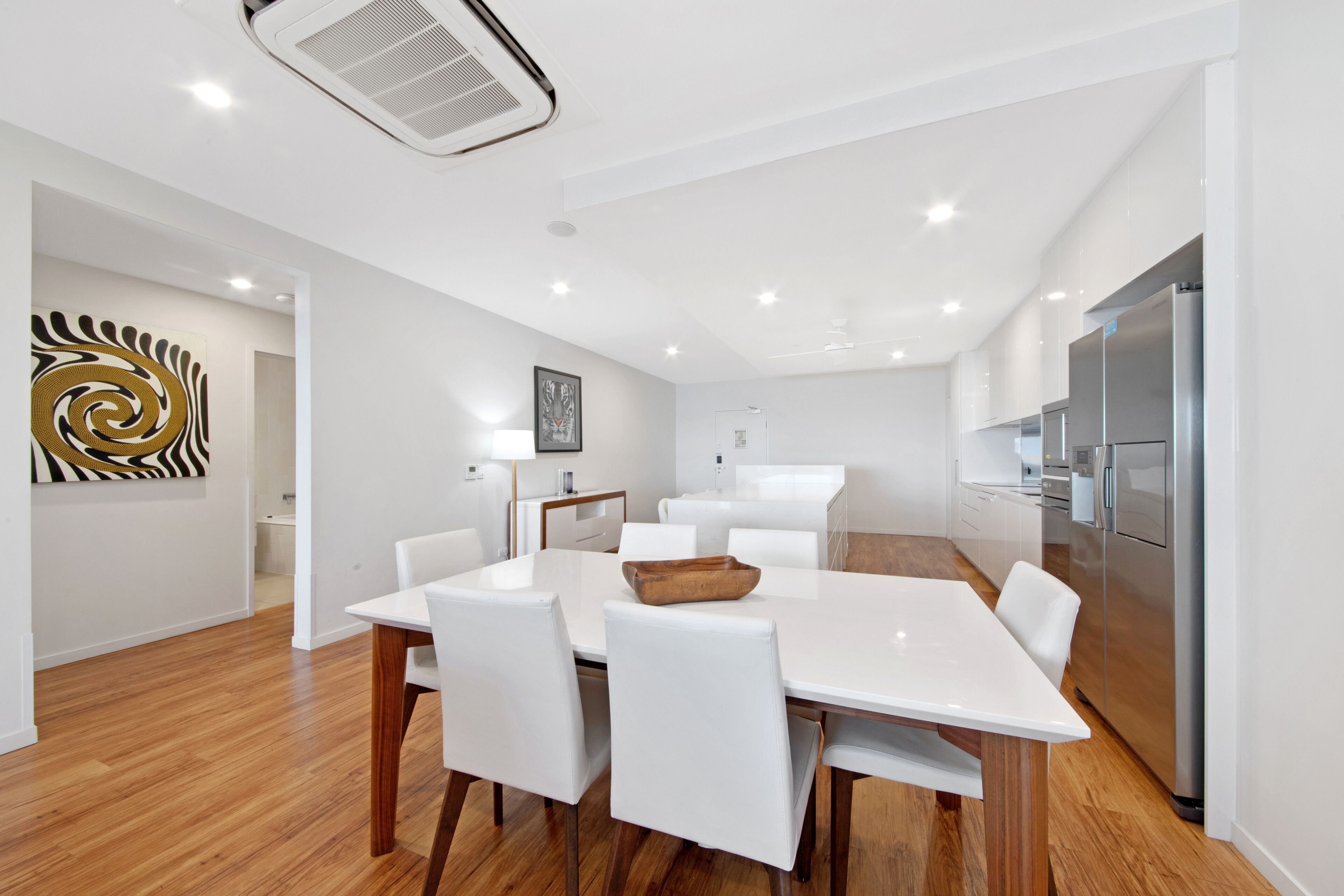 Una cocina moderna con muebles blancos, electrodomésticos de acero inoxidable y una mesa de comedor de madera con sillas blancas.