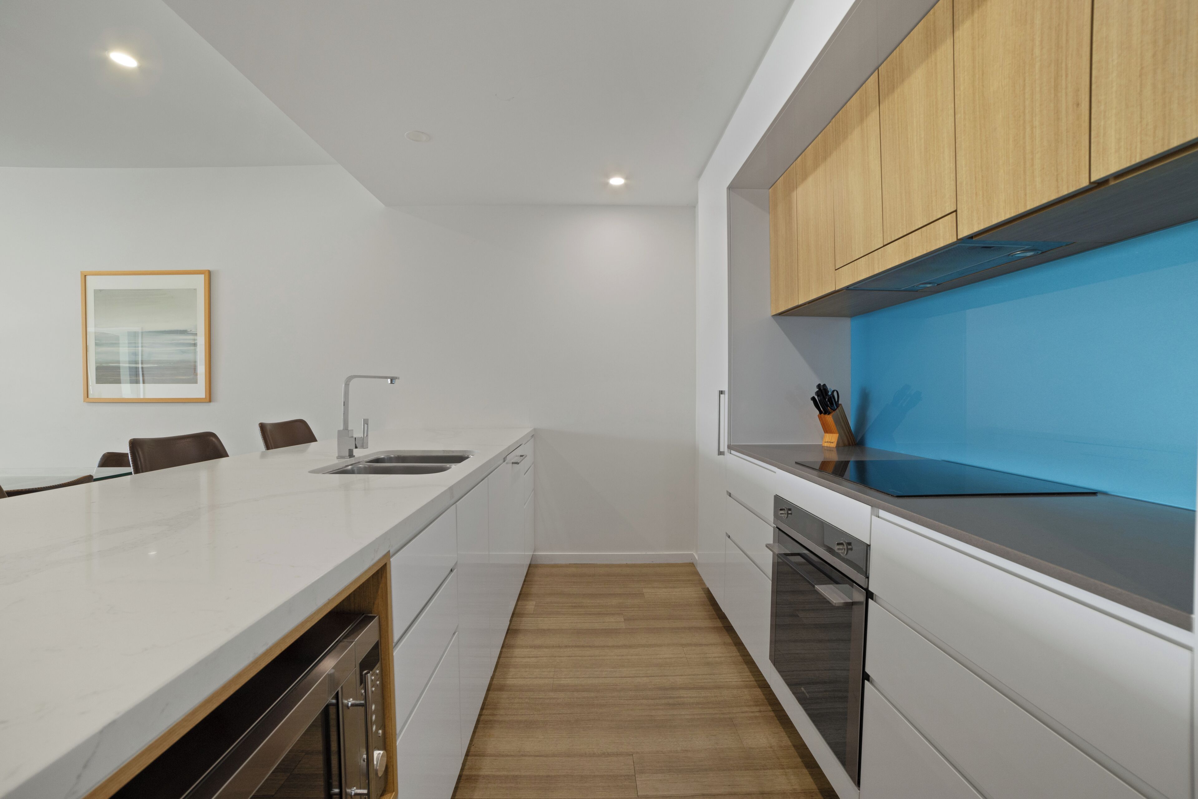 A modern kitchen with white cabinetry, a wooden countertop, and a blue backsplash.
