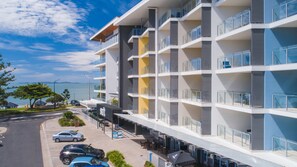 A multi-story hotel with balconies, a view of the sea, and a parking area with cars. - Salt Apartments Yeppoon (Yeppoon)