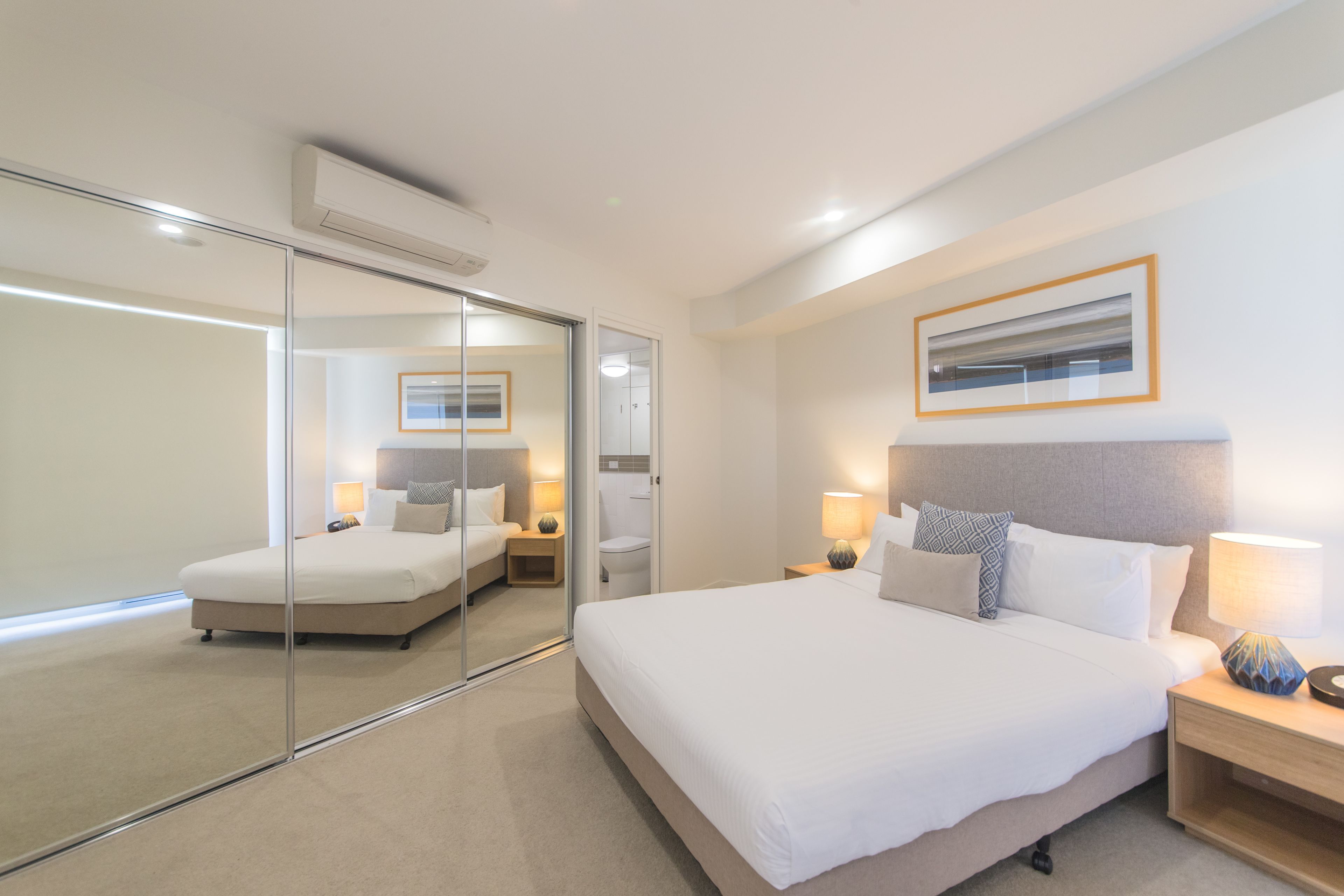 A modern hotel room with a large bed, bedside tables, a mirror, and a framed picture on the wall.