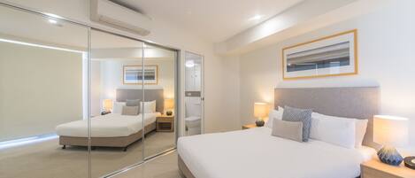 A modern hotel room with a large bed, bedside tables, a mirror, and a framed picture on the wall.