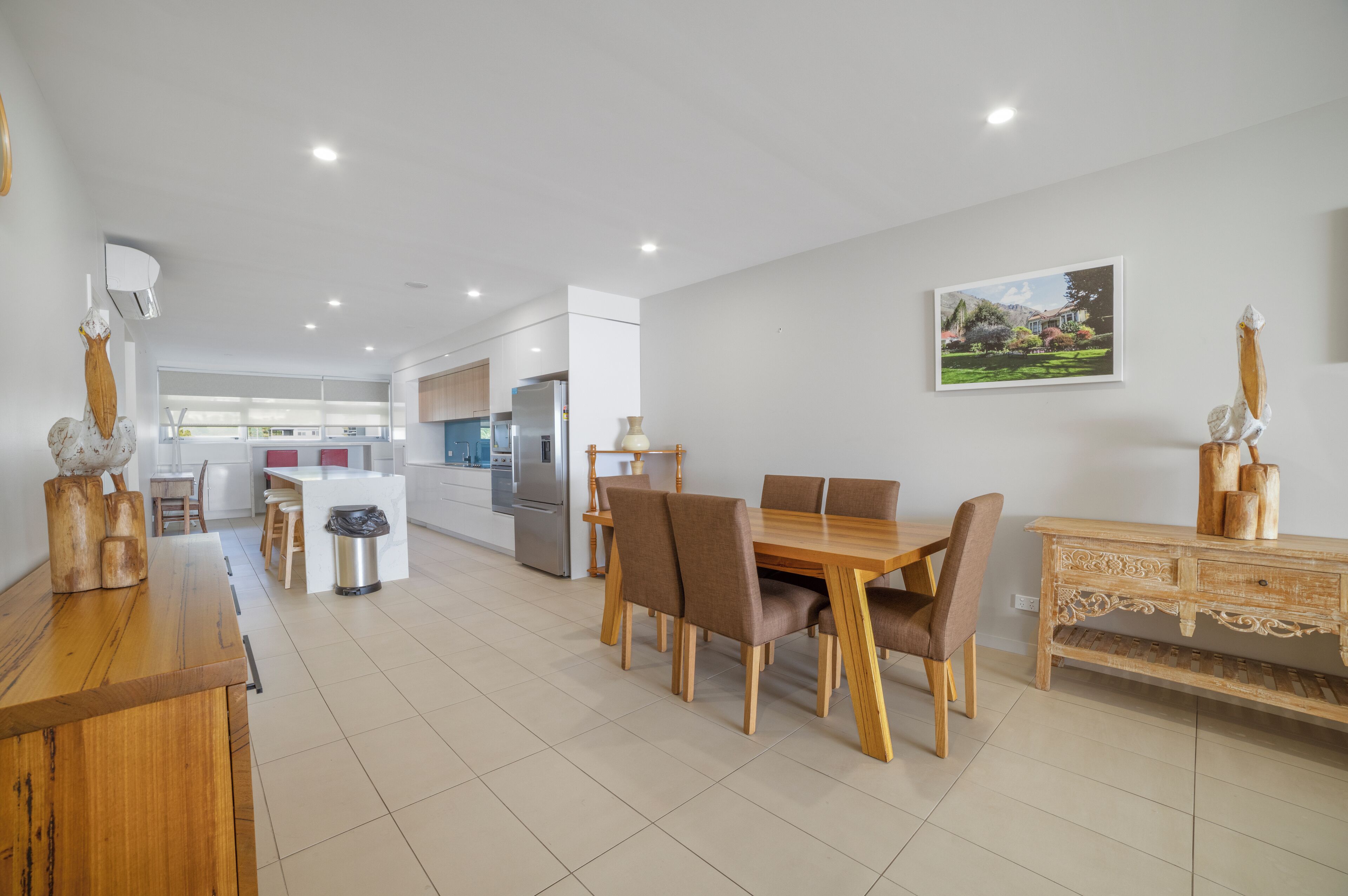 A modern kitchen with white cabinets, a dining area with a wooden table and chairs, and a decorative wooden cabinet with a vase.
