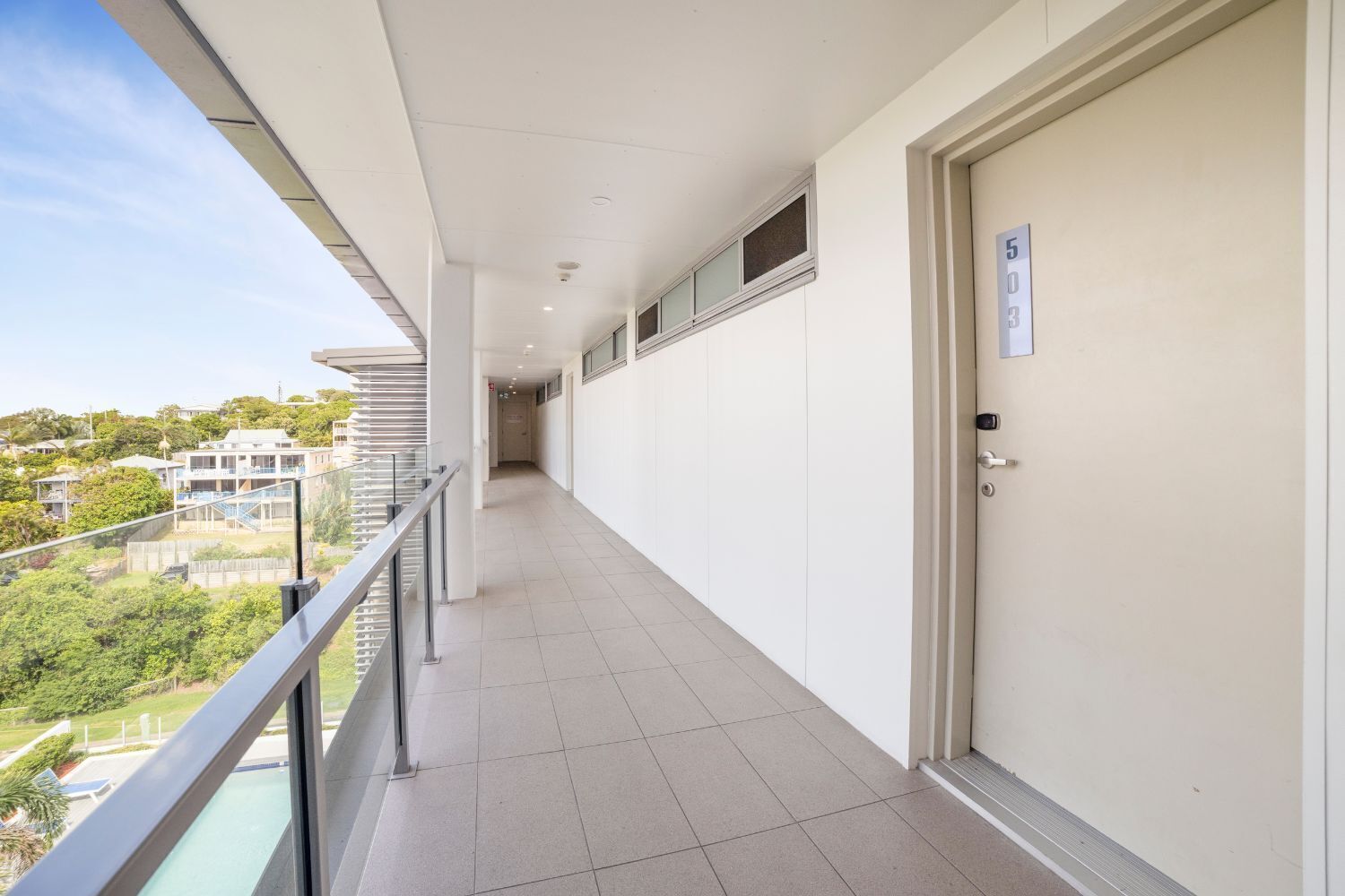 A long, narrow corridor with a glass balcony on one side, leading to a door marked with the number 5.