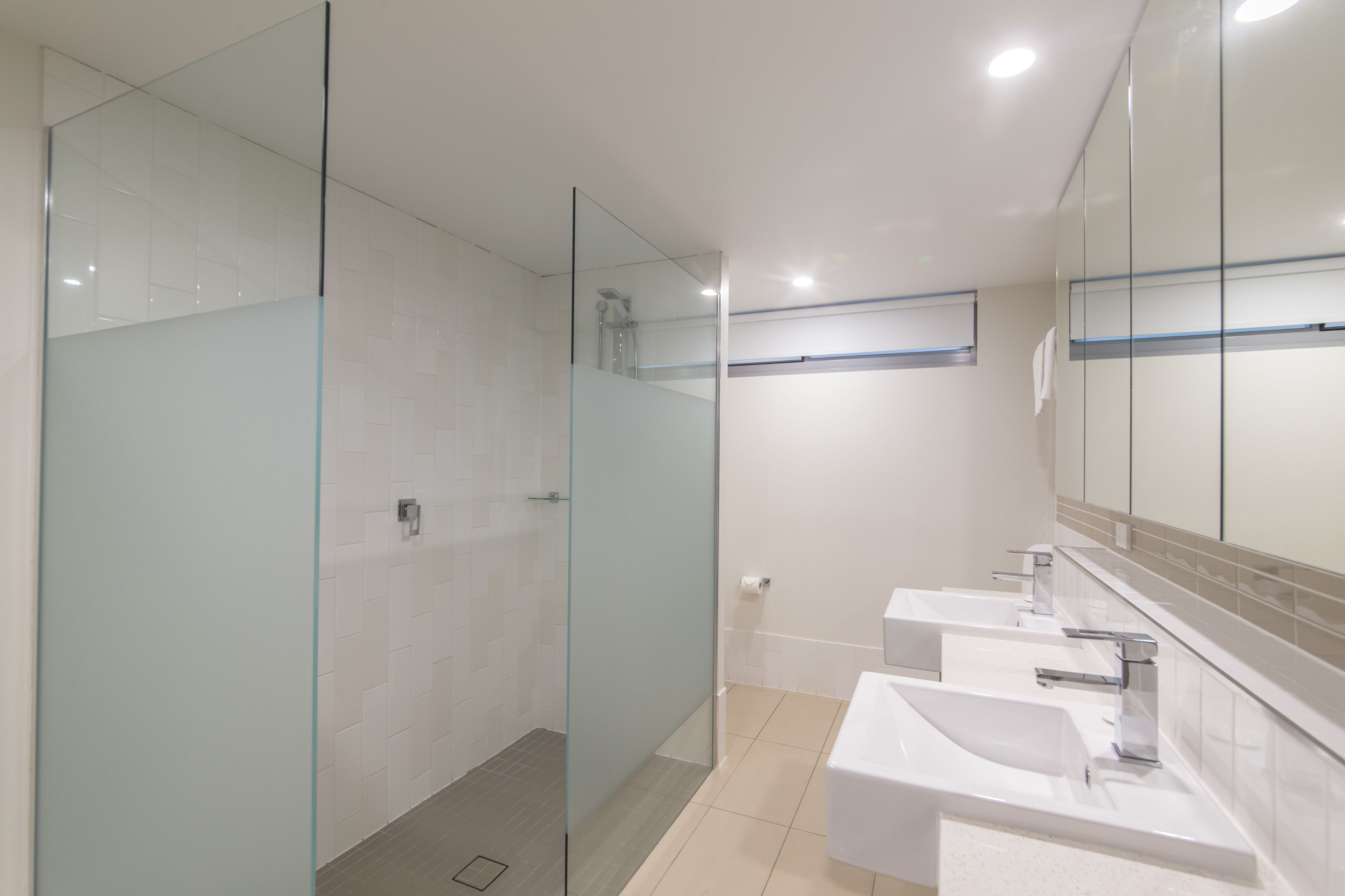 Ein modernes Badezimmer mit Glasduschtüren, einer bodengleichen Dusche und drei Waschbecken.