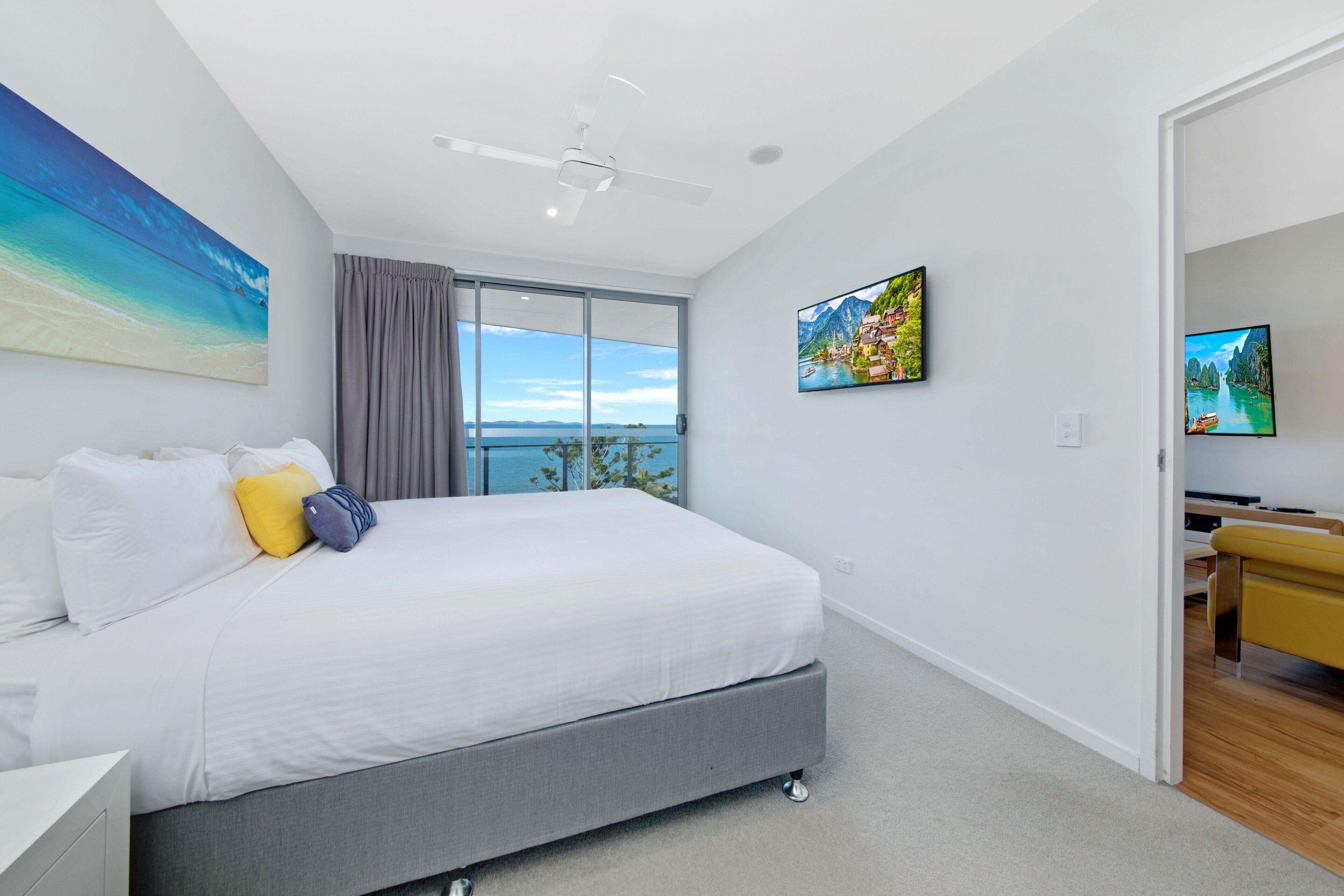 Une chambre moderne avec un grand lit, un ventilateur de plafond et une vue sur l’océan, accessible par une porte coulissante.