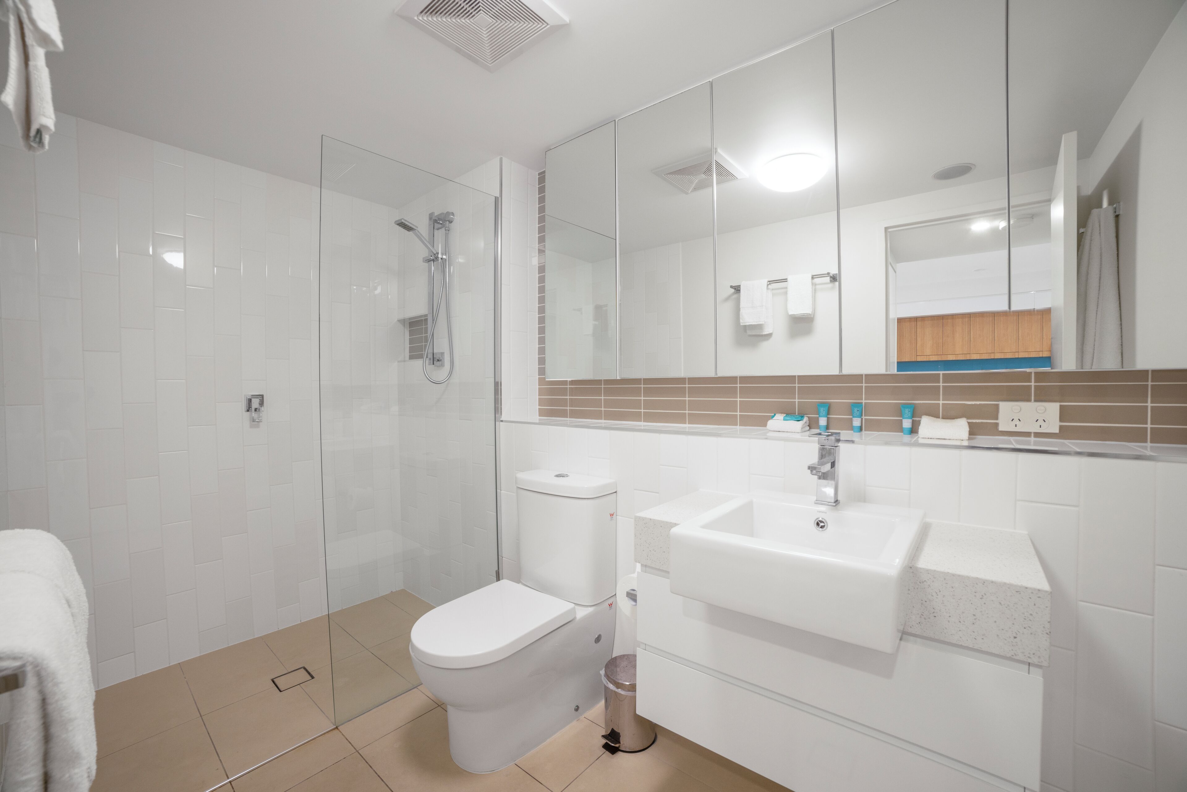 Une salle de bain moderne avec une douche à parois de verre, des toilettes blanches et un lavabo avec un miroir au-dessus.